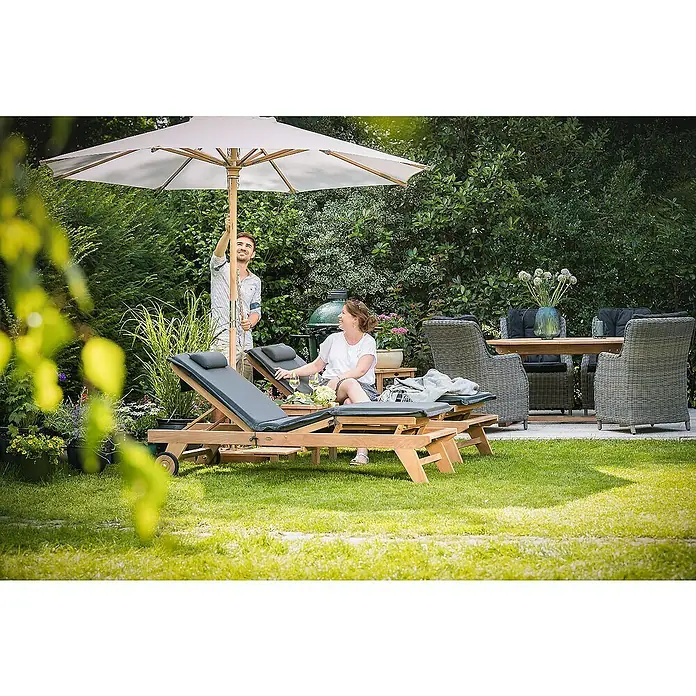 Kai Wiechmann Marktschirm - Ecru|Weiß|Natur|Beige - Gartenmöbel-Szene mit Sonnenschirm, Liegen und Essbereich. Eine Frau entspannt, während ein Mann den Sonnenschirm richtet.