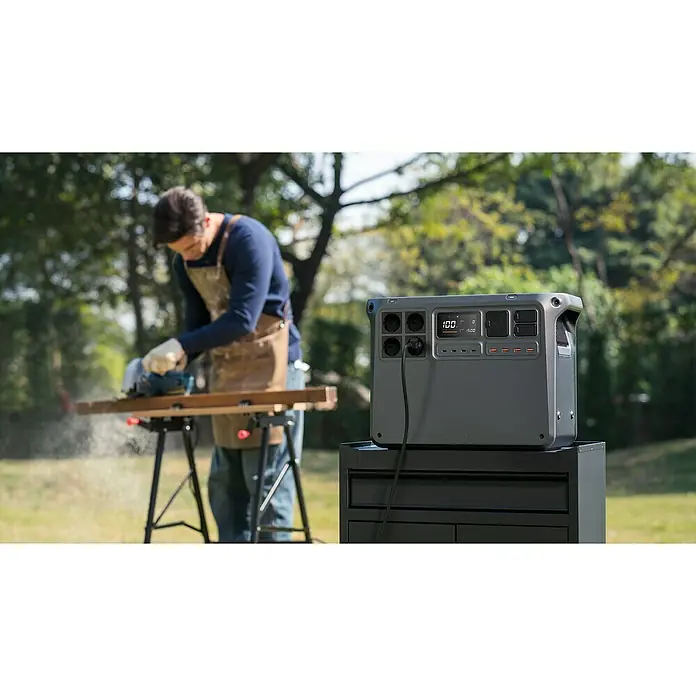 DJI Powerstation Power 2000 - 2.048 Wh, Schwarz - Ein tragbarer Stromgenerator mit 100 % Ladung steht im Freien, während eine Person mit einer elektrischen Säge an einem Holzstück arbeitet.