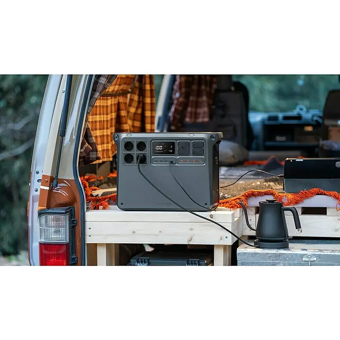 DJI Powerstation Power 2000 - 2.048 Wh, Schwarz - Power 2000 Stromgenerator im Heck eines Vans. Das Gerät lädt ein Tablet und versorgt einen Wasserkocher mit Strom, ideal für Camping.