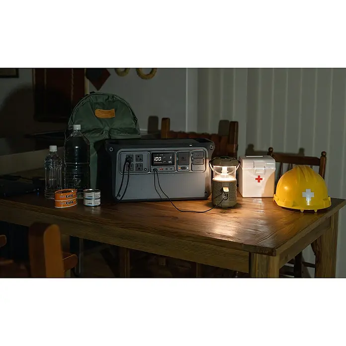 DJI Powerstation Power 1000 V2 - 1.024 Wh, Schwarz - Notfallausrüstung mit Powerstation, Lampe, Verbandszeug, Helm, Wasser und Konserven auf einem Tisch.