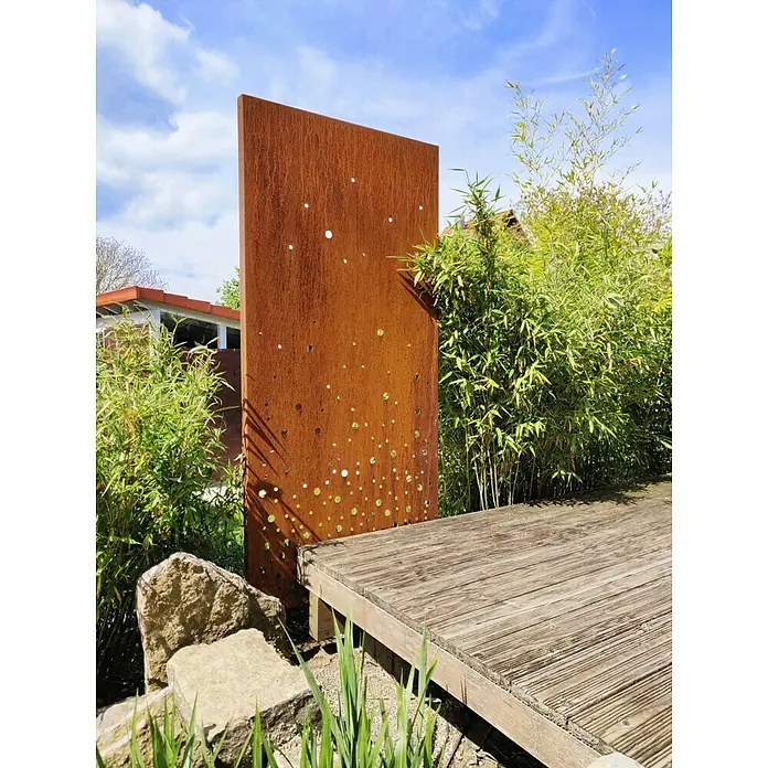 Palatino Space Vertical Sichtschutzelement Vapor - 87 x 180 cm, Edelrost, Vapor - Ein dekoratives, rotes Metallpaneel mit Lochmuster steht in einem Garten, umgeben von Pflanzen und einem Holzdeck.