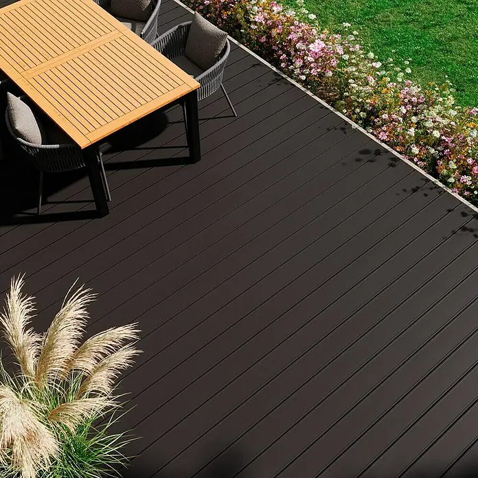 Kovalex WPC-Terrassendiele Massiv mit Struktur nach Maß - Graubraun, 310 x 14,5 x 2 cm - Eine moderne Terrasse mit dunklem Terrassendielen-Belag, einem Holztisch mit Stühlen und üppiger Bepflanzung, die ein stilvolles Ambiente schafft.