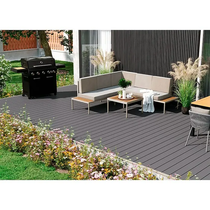 Kovalex WPC-Terrassendiele Massiv mit Struktur nach Maß - Grau, Unbehandelt, 580 x 14,5 x 2 cm - Eine stilvolle Außenterrasse mit Grill, Lounge-Ecke und blühendem Blumengarten für entspannte Stunden im Freien.
