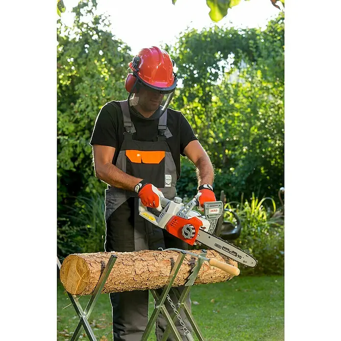 Ikra Akku-Kettensäge ICC 2/2035 - 40 V, 2 Ah, Li-Ionen, 2 Akkus - Ein Mann sägt mit einer IKRA Kettensäge ein Holzstück auf einem Sägebock, geschützt durch Helm und Handschuhe.