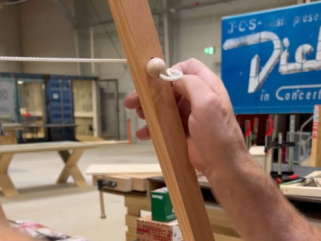 Ein Faden wurde durch das Loch in der Holzlatte gefädelt und eine Holzperle als Endstück raufgegeben