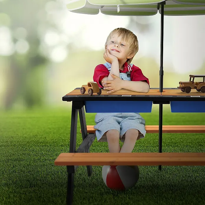 ML-Design Kinder-Picknicktisch Sitzgruppe inkl. 2 Wannen, Sand- und Wasserspieltisch Matschtisch - Braun, Blau, Schwarz, Holz - Ein Kind sitzt an einem Picknicktisch mit Sonnenschirm, umgeben von Spielzeugautos, perfekt für fantasievolles Spielen im Freien.