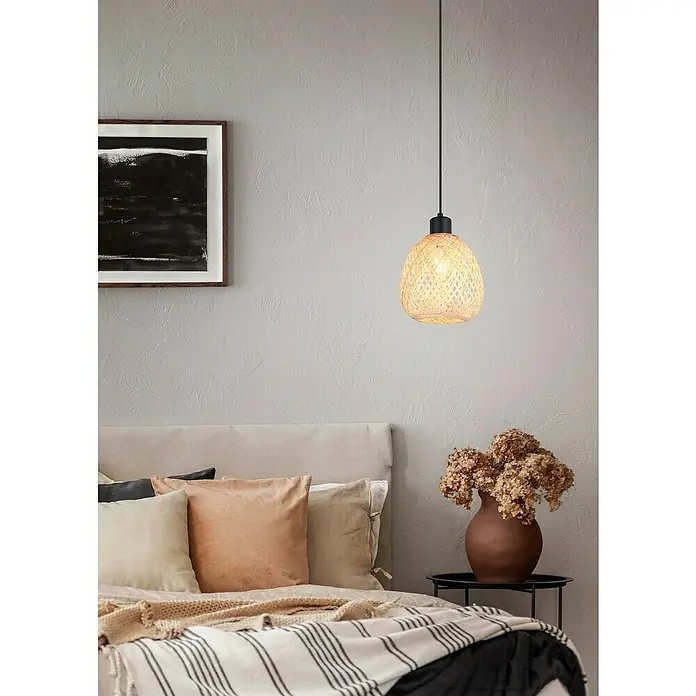 Trio Lighting Lámpara colgante redonda Amelie - 10 W, Ø x Al: 18 x 150 cm, Negro, E27 - Una lámpara colgante de ratán tejido cuelga sobre una cama con almohadas y una manta en un dormitorio.