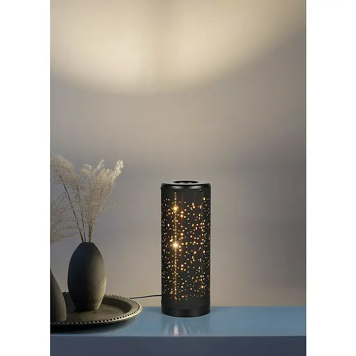 Reality Leuchten Tischleuchte rund Taco - Ø x H: 13 x 34,5 cm, Schwarz - Eine sternförmige Lampe auf einem Tisch mit einer Vase und einem Tablett, die ein warmes Licht in den Raum wirft.