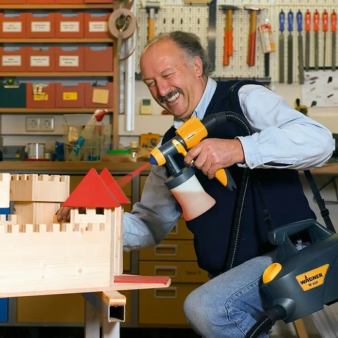 Wagner Sprühaufsatz Wood & Metal EXTRA Detail - Passend für: Wagner Farbsprühsystem Universal Sprayer & Wall Sprayer, Geeignet für: Dünnflüssige lösemittel- & wasserbasierte Materialien - Ein Mann sprüht mit einer Wagner Farbspritzpistole W 660 ein Holzschloss an. Perfekt für detaillierte Lackierarbeiten mit wenig Farbnebel.
