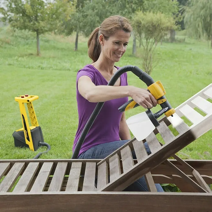 Wagner Farbsprühsystem W 950 Flexio - 630 W, Förderleistung: 0,525 l/min - Frau verwendet eine Wagner Farbspritzpistole zum Auftragen von Farbe auf eine Holzliege im Freien.