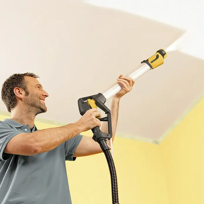 Wagner Farbsprühsystem W 950 Flexio - 630 W, Förderleistung: 0,525 l/min - Ein Mann streicht eine Decke mit einer Farbspritzpistole, wobei er die lange Lanze nutzt, um mühelos die Decke zu erreichen.