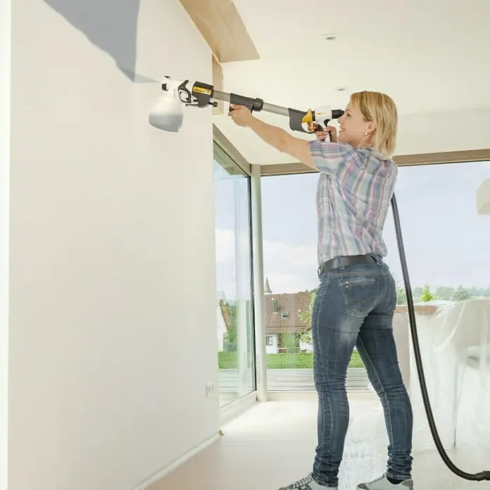 Wagner Griffverlängerung Universal EXTRA Extension - Länge: 60 cm - Frau benutzt eine Wagner Farbspritzpistole zum Streichen einer Wand. Das Gerät ermöglicht eine gleichmäßige Farbverteilung und spart Zeit beim Renovieren.