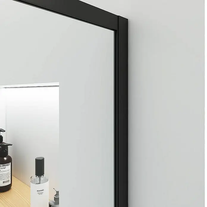Home Deluxe Duschwand BAKI - Schwarz / Klarglas - Nahaufnahme eines eleganten, rechteckigen Spiegels mit schwarzem Rahmen, der an einer weißen Wand hängt und modernes Design ausstrahlt.