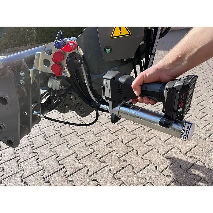 Mato Akku-Fettpresse Basic-S-LSP - 18 V, Ohne Akku, Max. Druck: 700 bar - Eine Hand bedient eine akkubetriebene Fettpresse, um ein landwirtschaftliches Gerät zu schmieren. Präzise Wartung für optimale Leistung.