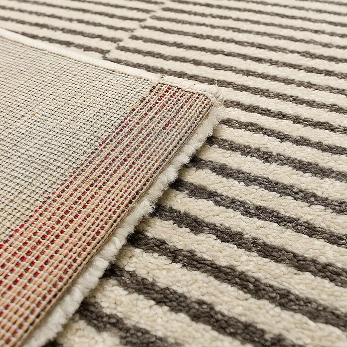 Dekoria Flachgewebeteppich - grau, creme, 170 x 120 cm - Detailaufnahme eines gestreiften Teppichs, der seine Rückseite mit Netzstruktur und roter Naht zeigt.\n