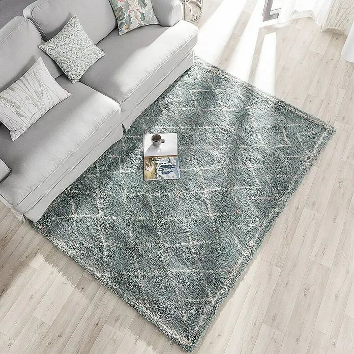 Dekoria Flachgewebeteppich - grün, 230 x 160 cm - Ein türkisfarbener Teppich mit Rautenmuster liegt unter einem Sofa mit Kissen und einem kleinen Tisch mit einer Tasse und einer Zeitschrift.