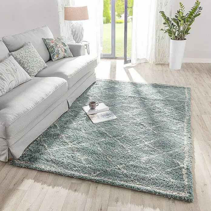 Dekoria Flachgewebeteppich - grün, 230 x 160 cm - Ein türkisfarbener Teppich mit geometrischem Muster liegt in einem hellen Wohnzimmer. Daneben ein Sofa und ein Beistelltisch.