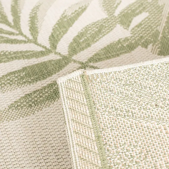 Dekoria Flachgewebeteppich - grün, beige - Nahaufnahme eines grünen Teppichs mit Blattmuster, der die Textur und das Design hervorhebt. Die Detailaufnahme zeigt die hochwertige Verarbeitung.
