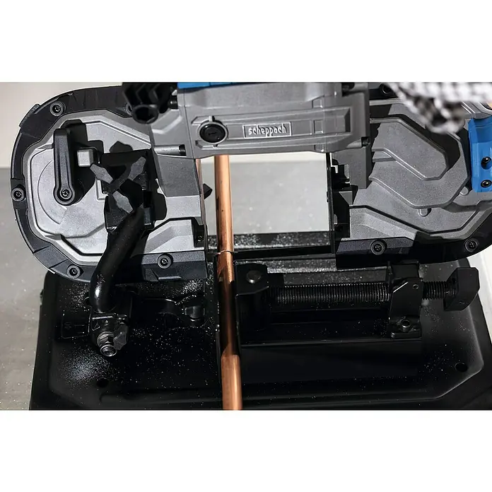 Scheppach Metallbandsäge MBS1200XT - 290 U/min, Schnittgeschwindigkeit: 0 m/min - 2,4 m/min, Sägebandlänge: 1.140 mm - Nahaufnahme einer Scheppach Metallbandsäge beim Schneiden eines Kupferrohrs, das im Schraubstock fixiert ist. Das Gerät ist auf einer Werkbank platziert.