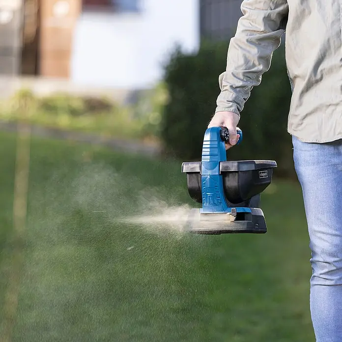 Scheppach IXES 20V Akku-Handstreuer C-GSP800-X Set S - 20 V, 2 Ah, 1 Akku - Ein Mann, der einen Scheppach Düngerstreuer im Garten benutzt, um Rasen zu düngen. Der Streuer verteilt Dünger gleichmäßig.