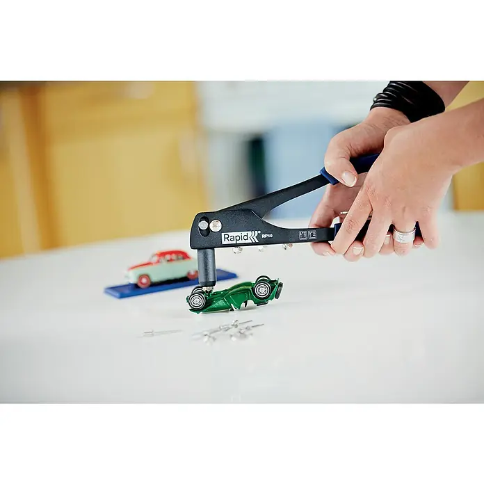 Rapid Blindnietzangen-Set RP10 - Geeignet für: Aluminiumnieten (Ø 3,2 mm, Ø 4 mm, Ø 4,8 mm) - Nahaufnahme einer Person, die mit einer Rapid RP10 Nietenzange an einem grünen Spielzeugauto arbeitet, mit Nieten auf einem weißen Tisch.