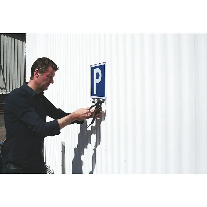 Rapid Blindnietzange RP110 - Geeignet für: Blindnietmuttern M3 - M6 - Ein Mann befestigt mit einem Nietwerkzeug ein blaues Parkplatzschild mit dem Buchstaben "P" an einer weißen Wand.