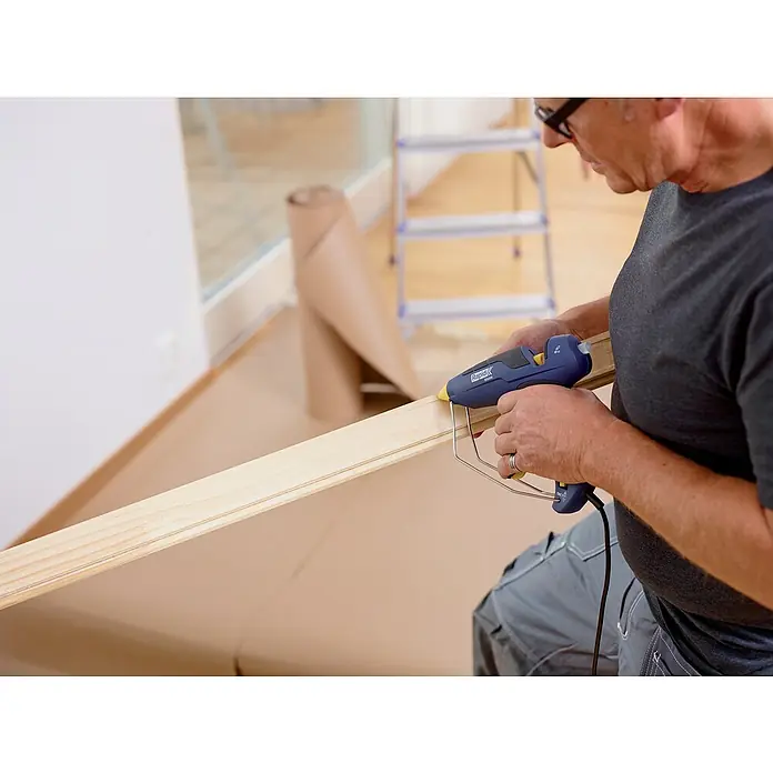 Rapid Heißklebepistole EG 280 - 350 W, Durchmesser Klebepatrone: 12 mm, 180 °C - 200 °C - Mann verwendet eine Rapid CG270 Akku-Klebpistole, um ein Holzstück mit Heißkleber zu befestigen. Im Hintergrund befindet sich eine Leiter.