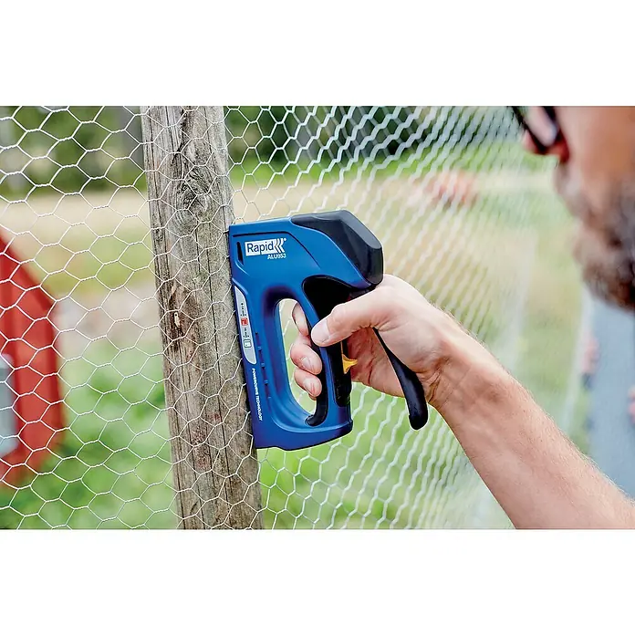 Rapid Handtacker ALU953 - Klammertiefe: 6 mm - 14 mm, Geeignet für: Klammern Typ 53 - Ein blauer Rapid ALU953 Tacker befestigt Drahtgeflecht an einem Holzpfosten. Er ist ergonomisch geformt für komfortable Anwendung.