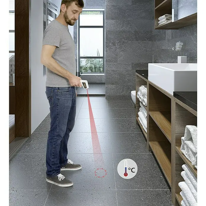 Laserliner Infrarot-Thermometer ThermoSpot Laser - Messbereich: -38 °C bis +365 °C - Ein Mann benutzt ein Infrarot-Thermometer zur Messung der Bodentemperatur im Badezimmer, mit Fokus auf die Gerätefunktionalität.