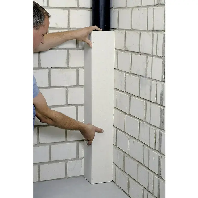 Fermacell Winkelelement - 1.000 x 150 x 150 mm - Mann befestigt eine weiße Abdeckung um ein schwarzes Rohr an einer weißen Ziegelwand.