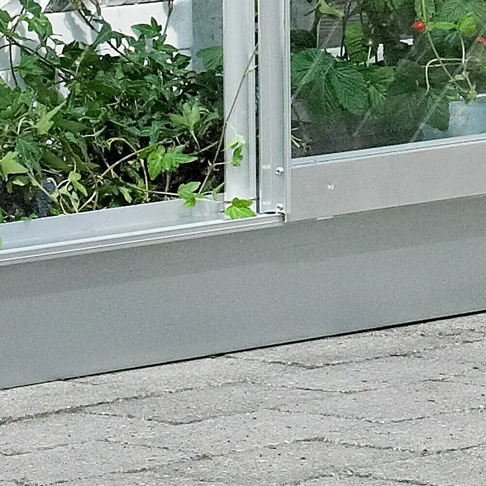 Juliana Gewächshaus-Fundament für Gewächshaus Altan - 0,69 x 1,32 x 0,12 m, Passend für: Halls Gewächshaus Altan 2 - Nahaufnahme eines Aluminiumgewächshauses, das eine Vielzahl von Pflanzen beherbergt und auf einem gepflasterten Untergrund steht.