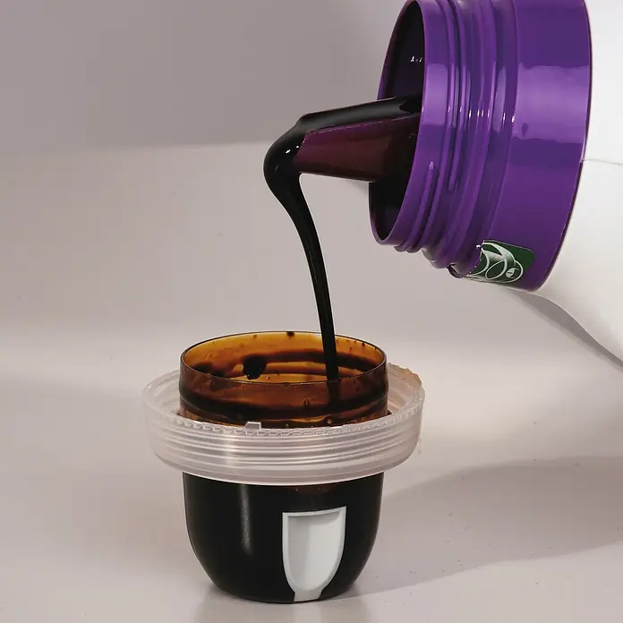 Compo Bio Blühpflanzendünger - 1,3 l - Ein dunkler Sirup wird aus einer lila Flasche in einen Messbecher gegossen, ideal für medizinische oder kulinarische Anwendungen.