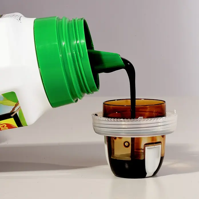 Compo Bio-Kräuterdünger - 0,5 l - Eine Flasche wird geneigt, um dunkle Flüssigkeit in einen Messbecher zu gießen.