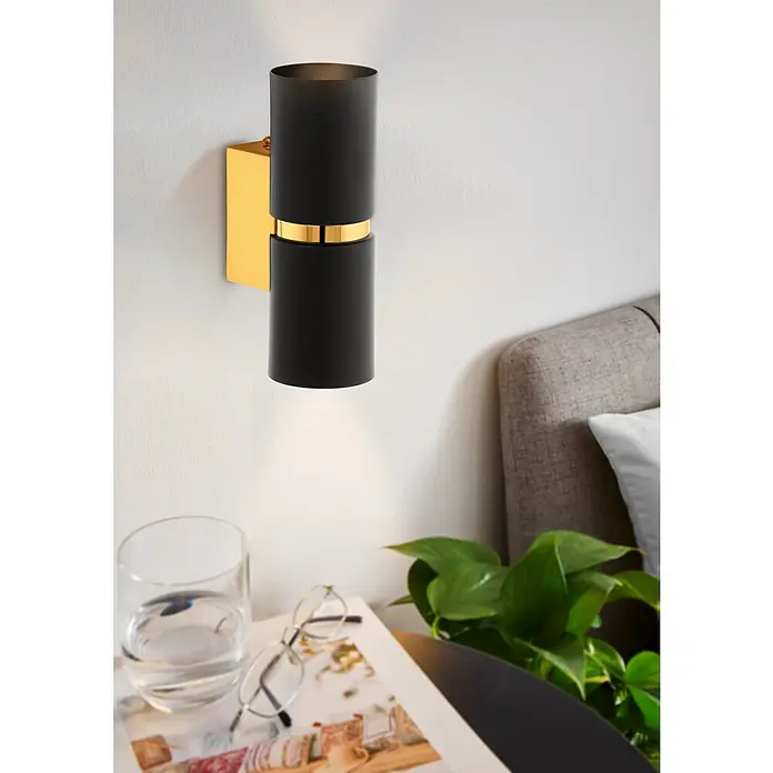 Eglo Aplique de pared Passa - 6 W, L x An x Al: 6 x 6 x 17 cm, Negro, GU10 - Primer plano de un aplique moderno negro y dorado junto a una mesita de noche con decoración.