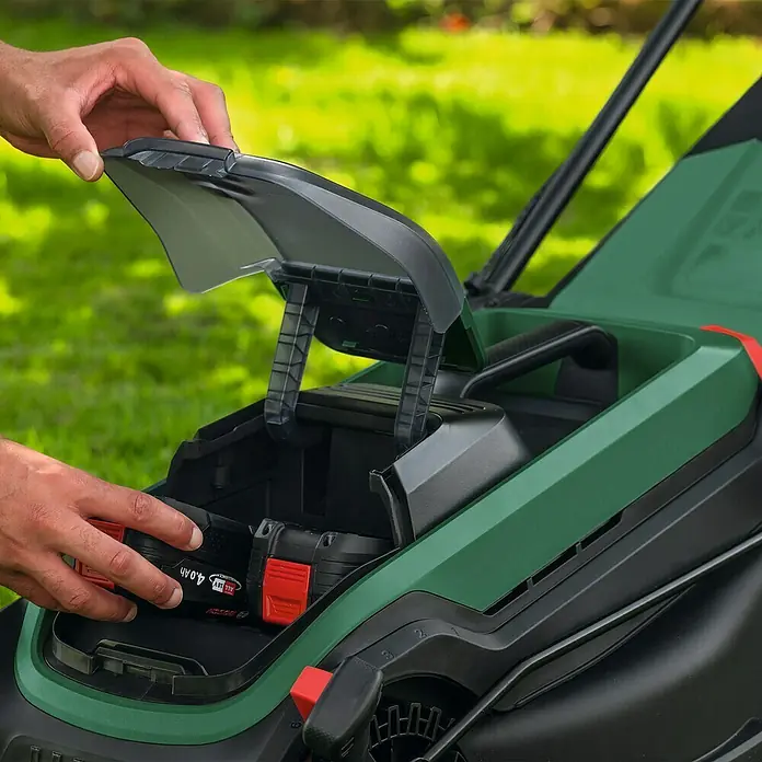 Bosch Power for All 18V Akku-Rasenmäher ROTAK18V2-38 - Ohne Akku, Schnittbreite: 38 cm - Nahaufnahme eines Akku-Rasenmähers, bei dem eine Hand den Akkufachdeckel öffnet, um einen Akku einzusetzen.