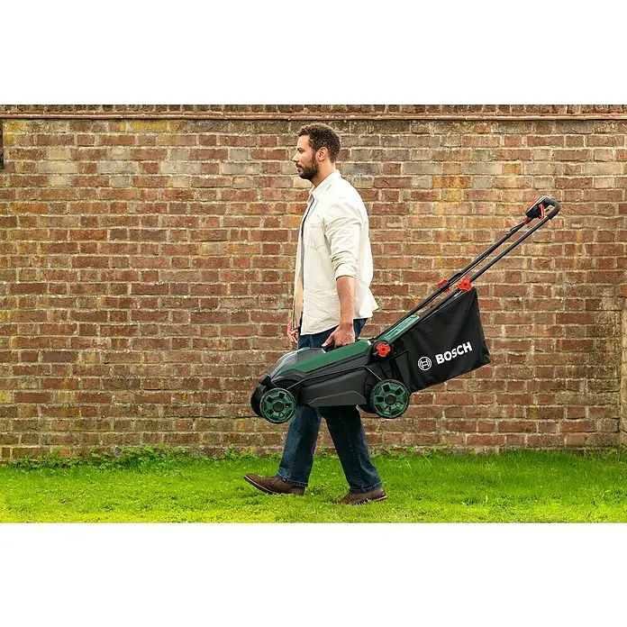 Bosch Power for All 18V Akku-Rasenmäher ROTAK18V2-38 - Ohne Akku, Schnittbreite: 38 cm - Ein Mann trägt einen Bosch-Rasenmäher vor einer Ziegelwand. Der Rasenmäher ist schwarz, grün und hat einen Fangkorb.