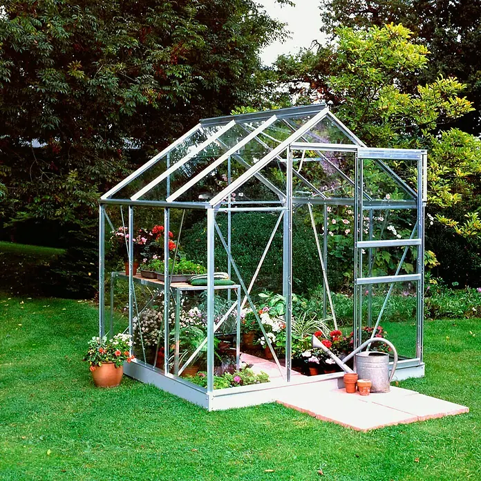 Halls Gewächshaus Popular 86 - Außenmaß inkl. Dachüberstand (B x T): 193 x 257 cm, Material Seitenwand: Glas, 3 mm, Silbergrau - Ein Gewächshaus aus Glas und Metall steht im Garten, gefüllt mit Blumen und Pflanzen, neben einer Gießkanne und Töpfen.