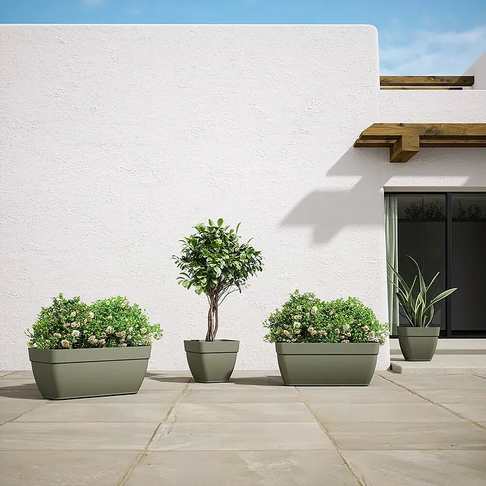 Artevasi Capri Campana Balkonkasten - Außenmaß (L x B x H): 79 x 37 x 33,5 cm, Kunststoff, Grau, Matt - Schönes Arrangement von vier grünen Pflanzgefäßen unterschiedlicher Größe mit Pflanzen auf einer Terrasse vor einer weißen Wand.