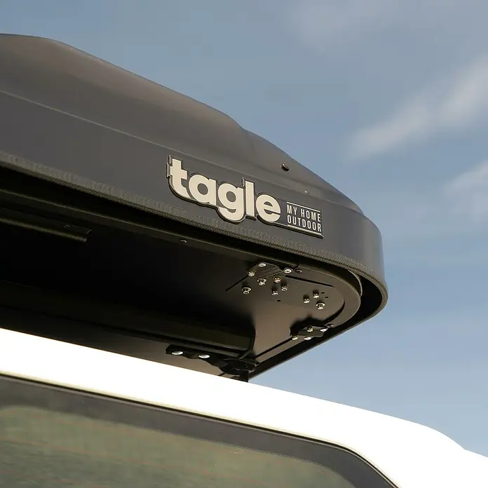 Tagle Outdoor Tienda de campaña para automóvil Hossegor + - Altura: 75 cm, Específico para: 2 personas, Apto para: 2 personas, Escalera telescópica - Primer plano de una caja de techo Tagle montada en un vehículo blanco, que ofrece almacenamiento adicional para aventuras de viaje al aire libre.