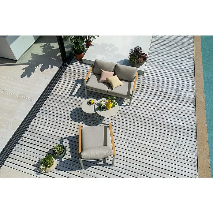 Sunfun Solo Loungesofa 2-Sitzer - B x T x H: 136 x 84,5 x 62,5 cm, Aluminium, Olefin, Light-Greige - Möbel-Set auf einer Terrasse mit einem grauen Sofa, einem Sessel und Beistelltischen. Pflanzen und ein Pool sind ebenfalls sichtbar.