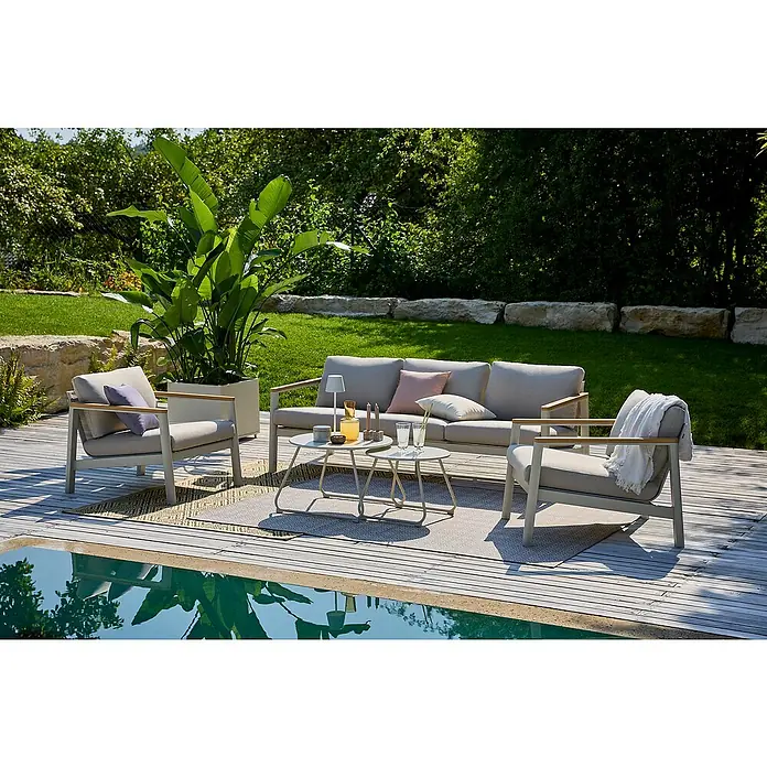 Sunfun Loungemöbel-Set Solo/Sarah - 5 -tlg., Aluminium, Stahl, Olefin, Light-Greige, 5 Stk. - Gartenmöbel-Set mit Sofa und Sesseln auf einem Holzdeck, neben einem Pool mit klarem Wasser. Die Möbel haben helle Polster und Holzarme.