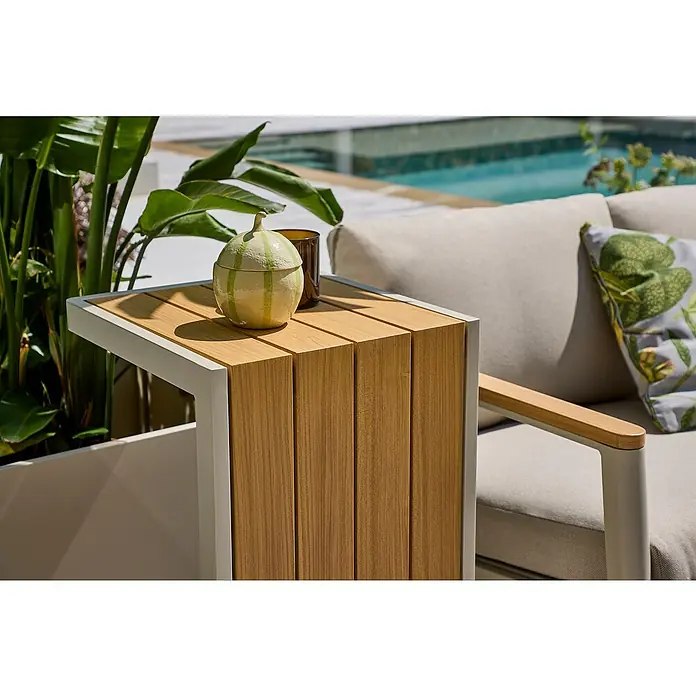 Sunfun Solo Garten-Beistelltisch - L x B x H: 73 x 38,5 x 41 cm, Aluminium, Leight-Greige - Nahaufnahme eines Beistelltisches mit Holzplatten und weißem Rahmen, daneben ein bequemes Sofa mit Kissen und eine Dekoration auf dem Tisch.