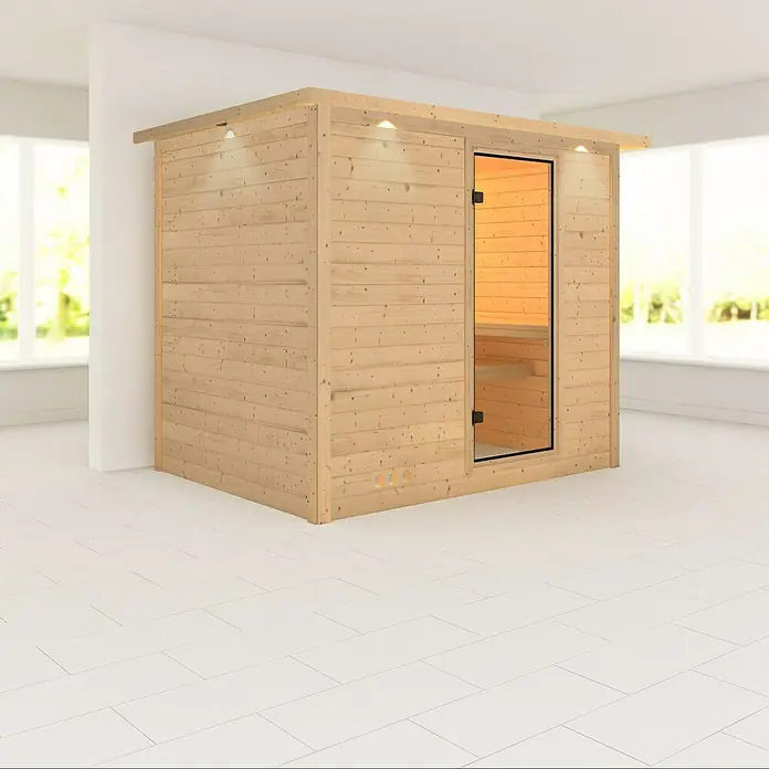 Karibu Massivholzsauna Sonara - Mit 9 kW Ofen mit externer Steuerung, Mit Dachkranz und Beleuchtung, L x B x H: 259 x 210 x 192 cm - Helles Holz Sauna mit Glasfront und Bänken im Inneren in einem hellen Raum.