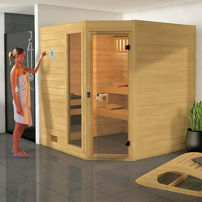 Weka Massivholzsauna Valida Eck 3 GTF - L x B x H: 189 x 239 x 203,5 cm - Diese Sauna mit Holzelementen und Glasfront lädt zum Entspannen ein. Die Frau im Handtuch bedient das Bedienfeld an der Wand der Sauna.
