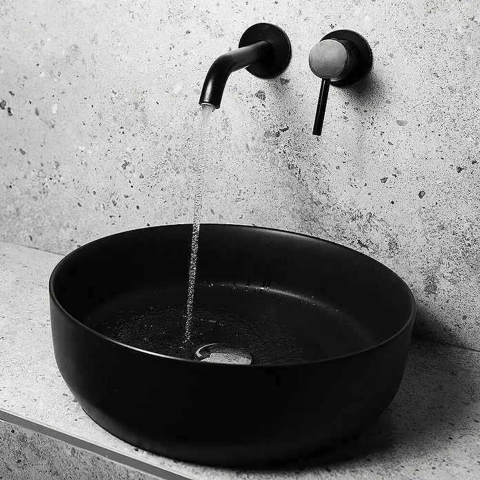LuxeBath Aufsatzwaschbecken Aufsatzwaschtisch Handwaschbecken Waschplatz Rund - 41,5 x 41,5 cm, Ohne Spezialglasur, Schwarz - Elegantes Waschbecken-Design: Eine moderne schwarze Schale mit stilvoller Armatur und fließendem Wasser vor einer strukturierten Wand.