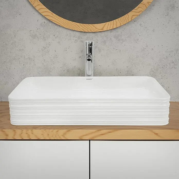 LuxeBath Aufsatzwaschbecken Handwaschbecken Weiß inkl. Ablaufgarnitur ohne Überlauf - Ohne Spezialglasur, Weiß - Rechteckiges Waschbecken mit geriffelter Außenseite auf einem Holzunterschrank, darüber ein runder Spiegel und eine Armatur.