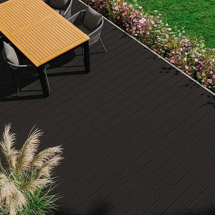 Kovalex WPC-Terrassendiele Exklusiv nach Maß - Graubraun, Gebürstet, 400 x 14,5 x 2,6 cm - Einladende Terrasse mit edlem Esstisch und Stühlen, umgeben von üppigen Blumen und dekorativem Gras auf dunklem Terrassenboden.