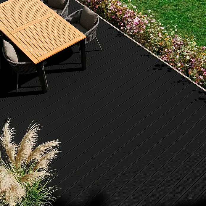 Kovalex WPC-Terrassendiele Exklusiv nach Maß - 410 x 14,5 x 2,6 cm, Anthrazit - Ein stilvolles Gartendeck mit schwarzen Dielen, ergänzt durch einen Esstisch und Stühle, umgeben von üppigem Grün und Blumen.