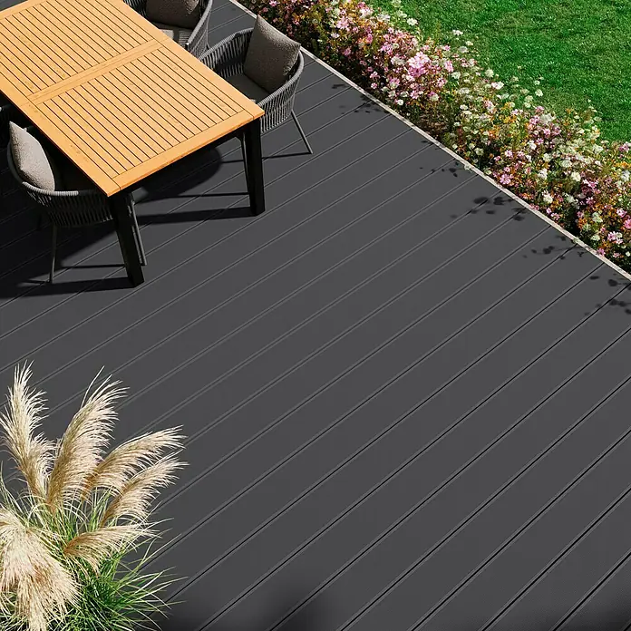 Kovalex WPC-Terrassendiele XL mit Struktur nach Maß - Steingrau, 370 x 19 x 2 cm - Bild einer modernen Terrasse mit dunkelgrauen Dielen, Gartenmöbeln und üppiger Bepflanzung. Die grauen Dielen verleihen der Terrasse einen modernen Look.