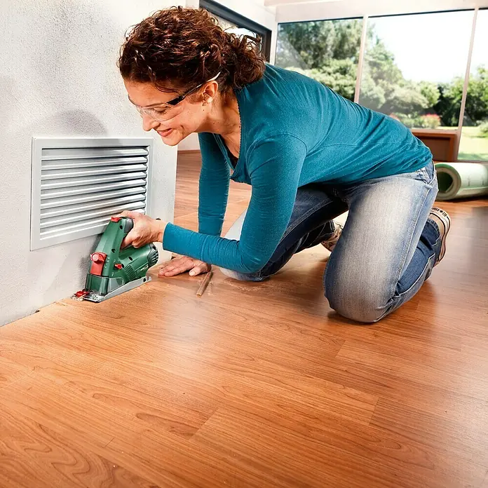 Bosch Handkreissäge PKS 16 - 400 W, Durchmesser Sägeblatt: 65 mm - Frau schneidet mit einer Bosch-Säge Laminatboden in einem Raum.